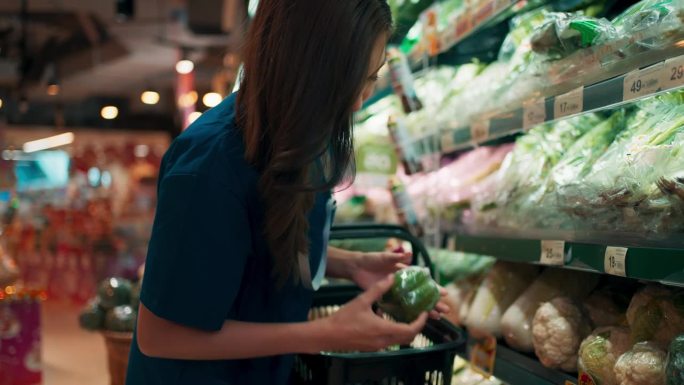 穿着医疗服的年轻漂亮的亚洲医疗技术员在超市购物，拿着购物篮的医疗人员在商店挑选水果和蔬菜