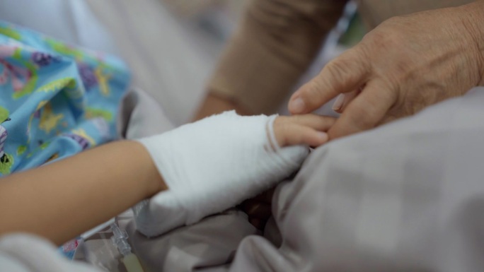 一位老妇人在病床上握着孙子的手，希望他早日康复。