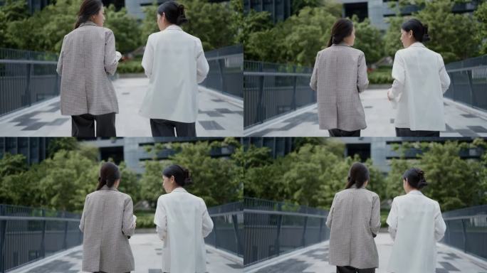 两个亚洲女商人一起走在环境优美的现代办公大楼的后视图。