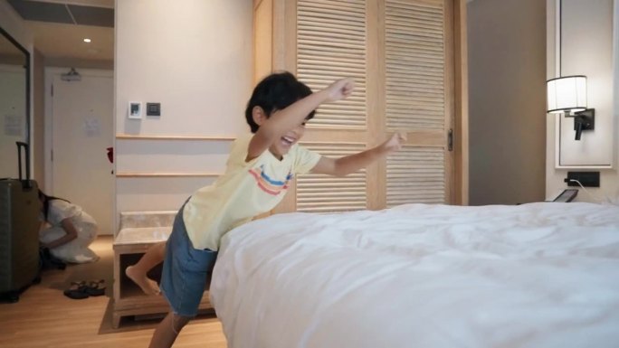 幸福的年轻家庭带着孩子走进豪华酒店的房间，孩子在床上跳来跳去。