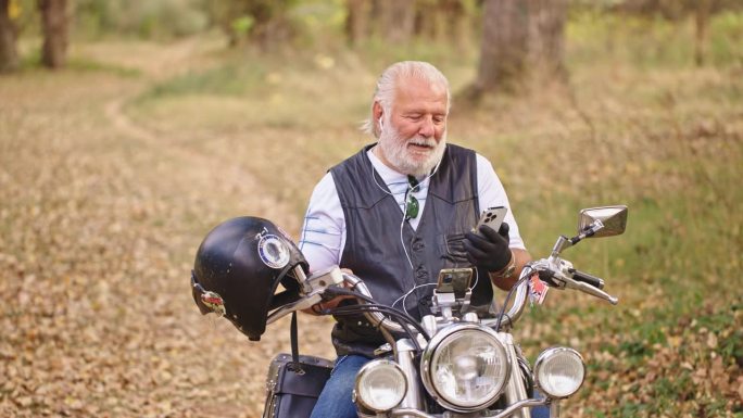 开朗的年长男性白种人骑摩托车，坐在摩托车上，用耳机通过视频通话打电话