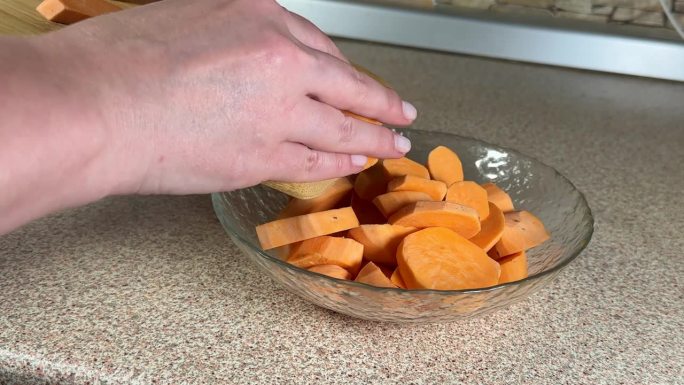 一个女孩正在做一个橙色的红薯，她把一块木板上的蔬菜倒进盘子里
