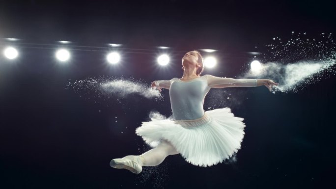 一位才华横溢的芭蕾舞演员在舞台上表演的肖像。年轻的女性在一个黑暗的工作室里做一个劈开跳跃和从她的手中