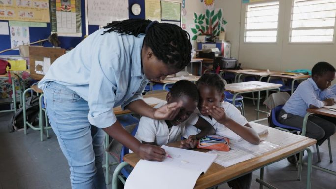 特写镜头。在非洲的一间教室里，非洲黑人女教师站在讲台上帮助非洲孩子画画