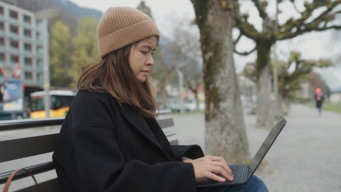 自由职业者坐在公园里的金属椅子上，一边在城市里旅行，一边用电脑工作。