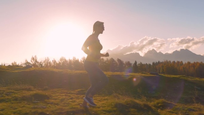特写，镜头光晕:穿着运动服的运动女子在长满草的山脊上奔跑