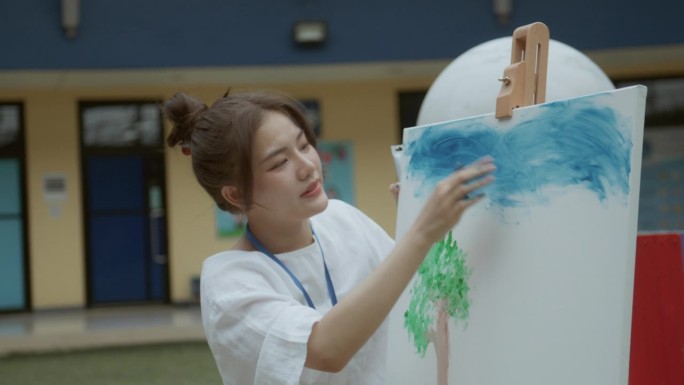 亚洲年轻成年女教师在学校操场的美术课上给多种族小学生讲授丙烯画。