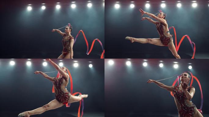 一个现代艺术体操表演的超级慢动作镜头在一个大舞台上的灯光。美丽的女运动员在用红丝带创造形状的同时做出