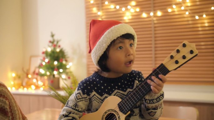 圣诞节那天，一个小男孩喜欢和家人在装饰精美的客厅里弹吉他唱歌。