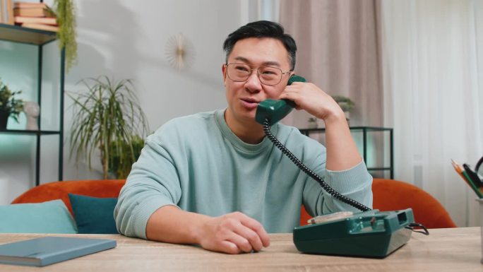 一个亚洲人在家里的沙发上和朋友打90年代的复古电话