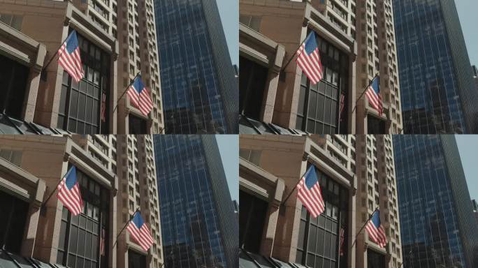 两面美国国旗悬挂在纽约市一座现代玻璃摩天大楼旁的纪念性历史建筑上。
