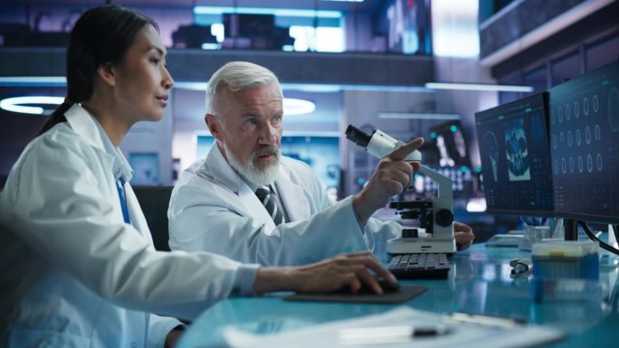 生物技术医学研究中心:亚洲女性神经科医生用台式电脑与白人男性科学家用显微镜交谈。医生研究阿尔茨海默病