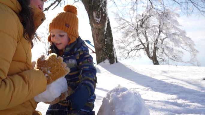 蹒跚学步的小男孩帮妈妈堆雪人