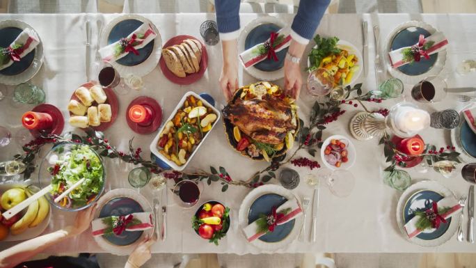 高雅装饰的圣诞宴会桌烤火鸡，蔬菜配菜，烤土豆，甜点。从上往下看，人们把盘子放在家里的餐桌上