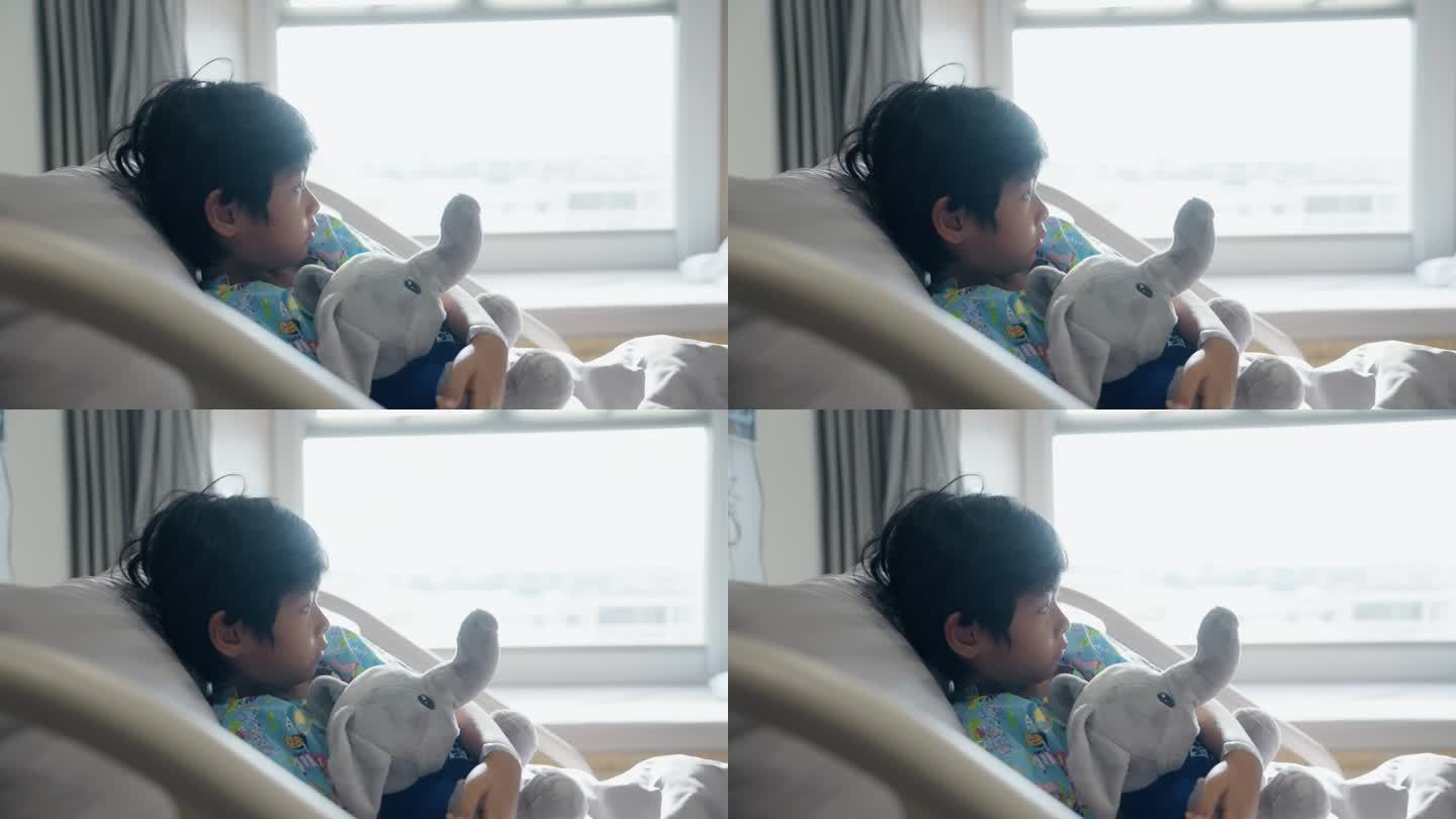 周末，一名带着大象娃娃的亚洲男孩躺在医院的病床上。