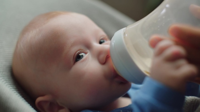男婴吮吸奶瓶，小孩子吃，婴儿食品概念和握着妈妈的手