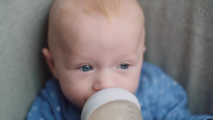 在家用奶瓶给小男孩喂奶，肖像婴儿宝宝吃、喝奶粉。