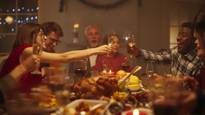 一位英俊的非洲青年在圣诞餐桌上敬酒。家人和朋友一起吃饭，举杯共饮香槟，敬酒，庆祝寒假