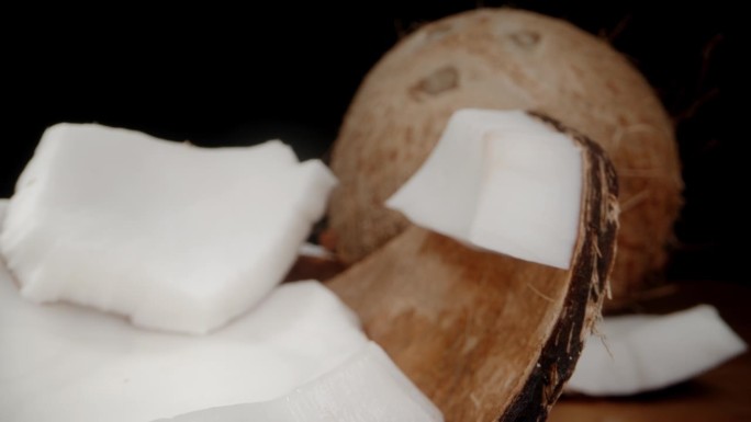 白色的果肉在椰子上，壳碎片在桌子上，背景是一个完整的椰子。多莉滑块极端特写。