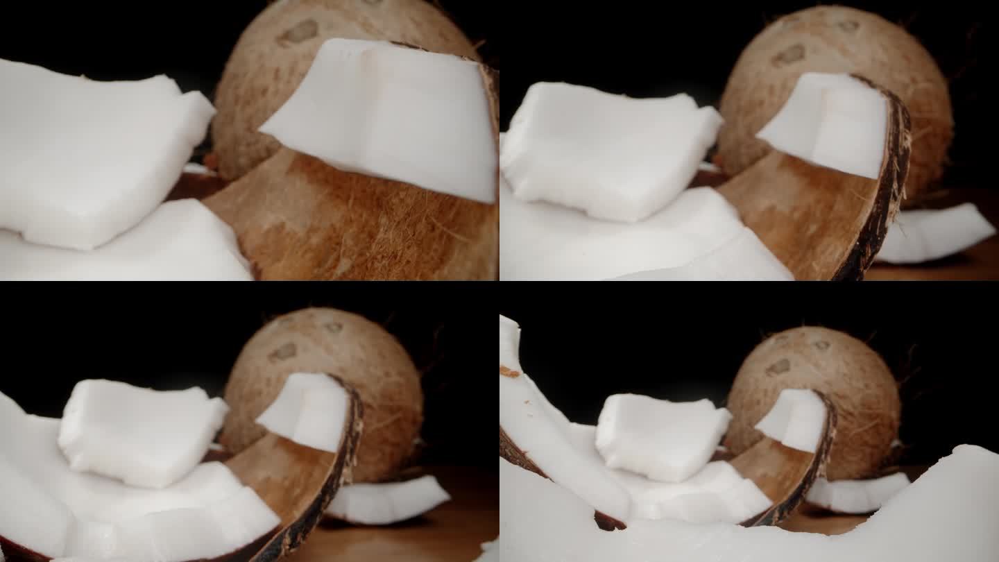 白色的果肉在椰子上，壳碎片在桌子上，背景是一个完整的椰子。多莉滑块极端特写。