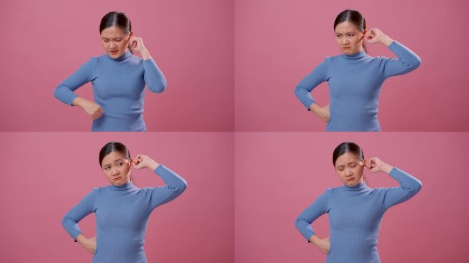亚洲女人耳朵发痒，把一个手指放进耳朵里，孤立地站在粉红色的背景上。
