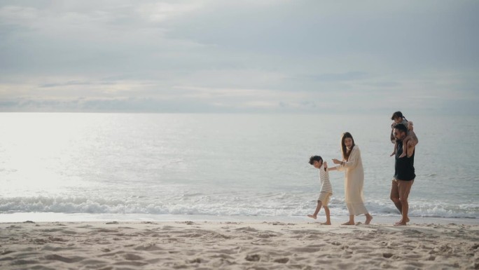 幸福的一家人在暑假日落时漫步在海滩上。