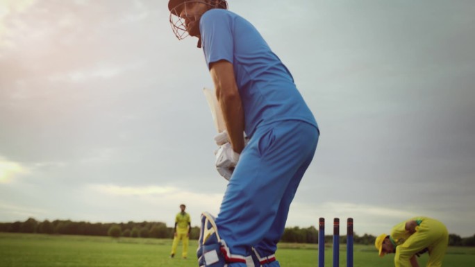 一个职业击球手的肖像集中在他成功击球之前。英俊的板球运动员穿着蓝队制服和头盔，站在夕阳球场