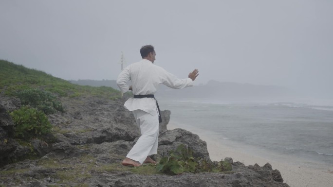 一名男子在沙滩上慢镜头练习空手道技巧