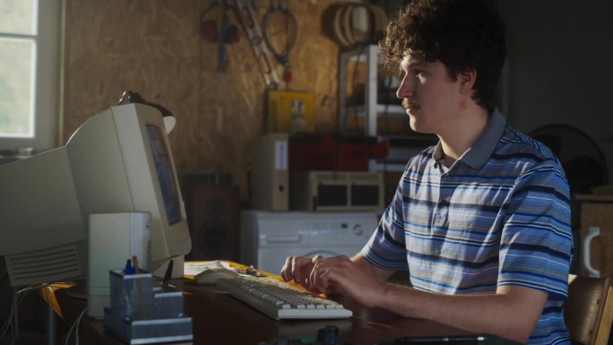 白人男性软件工程师在复古车库的旧台式电脑上用随机的电器编程。男子在90年代创办了一家创新的电子商务创