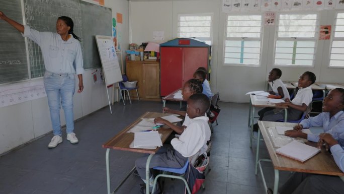 特写平移视图。非洲黑人女教师站在黑板前，在非洲的一间教室里给孩子们上课