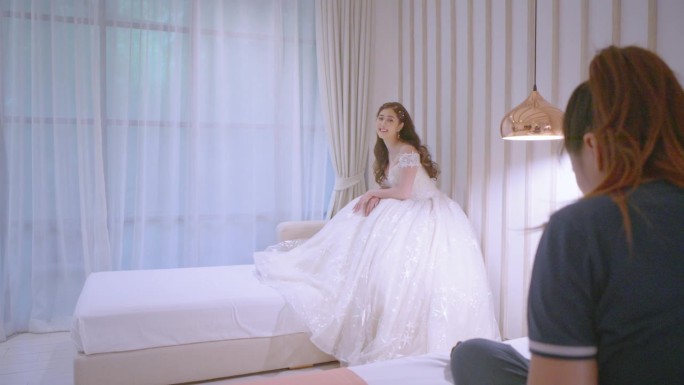 当新娘坐在酒店房间的沙发上时，摄影师正在给她拍照。”