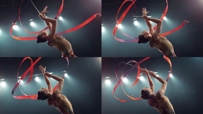 灯光大舞台上的现代艺术体操表演。一位美丽的女运动员手持红丝带跳舞的肖像。电影超级慢动作速度斜坡效果