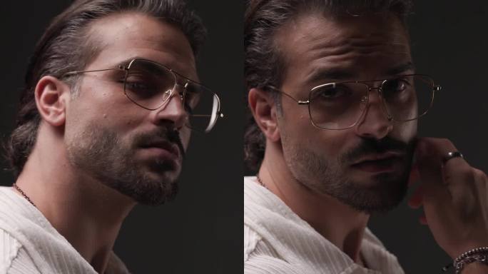 侧视图视频，性感的大胡子男子带着眼镜看向一边，触摸脸，在灰色背景的闪光灯前很有诱惑力