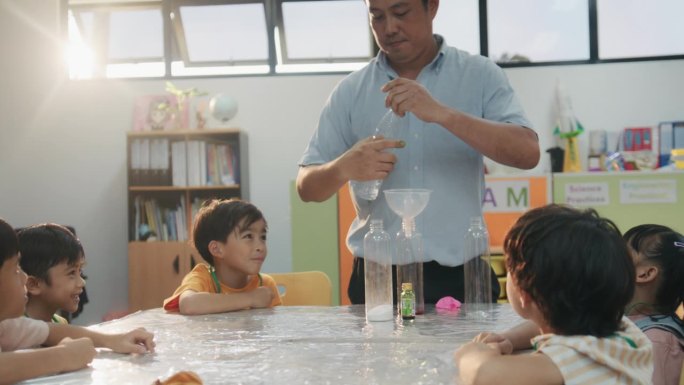 亚裔男老师在教室里与小学生们一起讲解小苏打的化学反应。