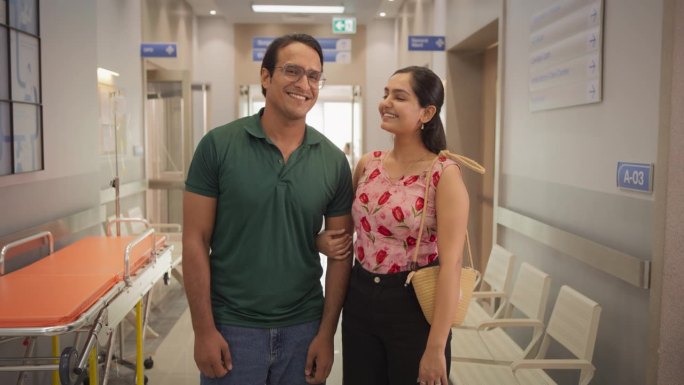 年轻的印度夫妇在医院微笑着看着镜头的肖像。快乐的男性和女性患者对现代地方医疗诊所提供的保健服务感到满