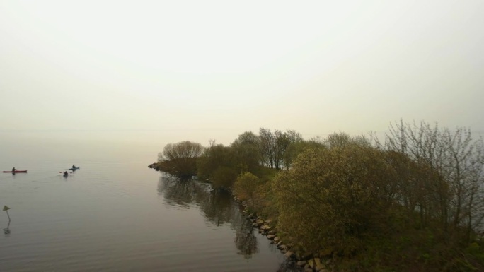 无人机拍摄的画面显示，人们在雾气笼罩的宁静湖泊附近的小半岛上划桨