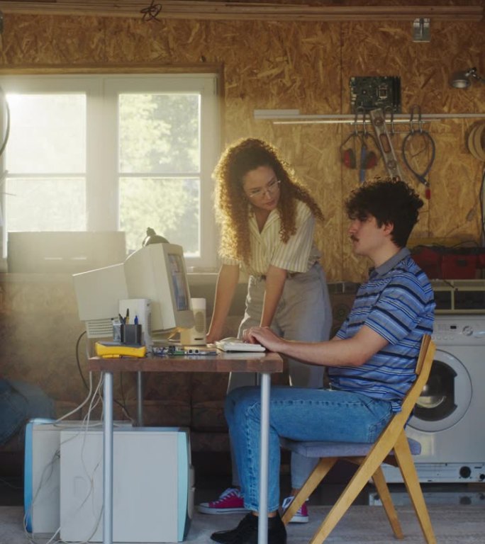 垂直屏幕:白人男性软件开发人员和西班牙裔女性设计师在复古车库谈论和使用旧台式电脑。90年代不同的创业