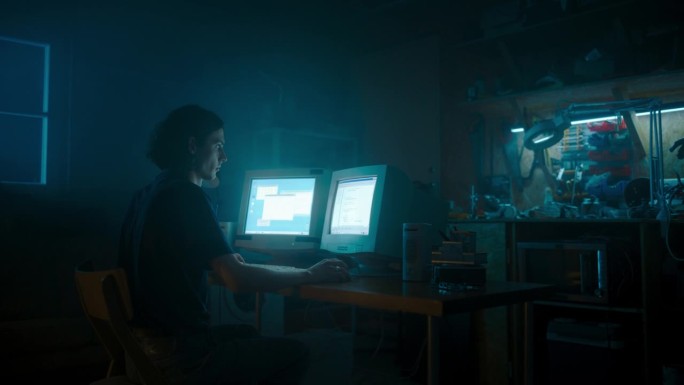 白人男性程序员深夜在复古车库使用带两个显示器的旧台式电脑。邪恶的黑客搜索软件漏洞，编码DDOS攻击，