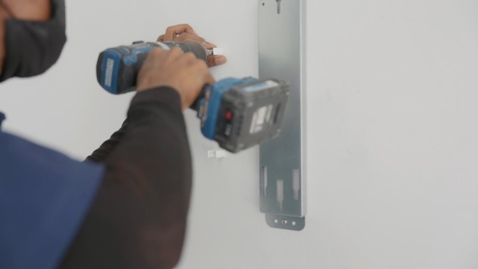 一名亚洲男子用无绳钻在墙上钻螺丝，为公寓安装电力系统