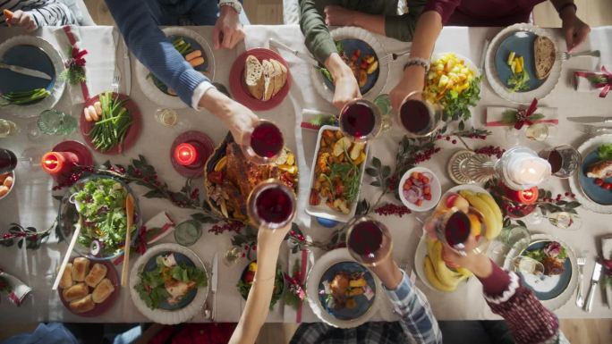 父母，孩子和朋友在一个舒适的家一起享受圣诞晚餐。亲戚们一起吃饭，举杯喝红酒，举杯祝酒，庆祝节日。自顶