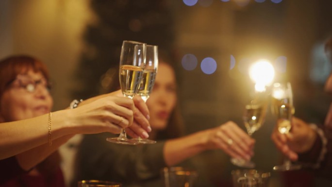 父母，孩子和朋友们举着香槟，举杯，庆祝寒假的特写。客人们在一个舒适的家一起享受圣诞晚餐
