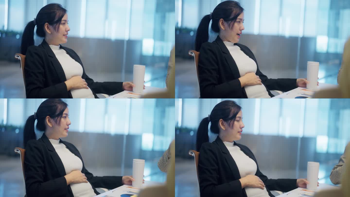 亚洲怀孕经理坐在桌边的侧视图在办公室工作时头脑风暴和揉肚子。