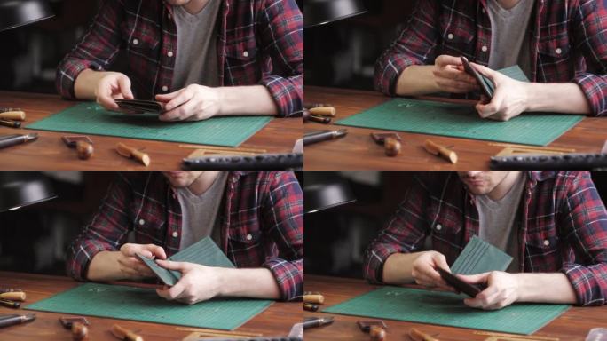 男裁缝用尺子裁剪人造革特写。工匠在工作桌上雕刻牛皮，制作用真皮制作的手工制品。专业的工作室。