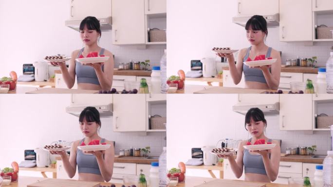 一个爱运动的亚洲女人陷入了两难的境地，在她的厨房里，她决定是沉迷于一盘诱人的甜点，还是选择更健康的水