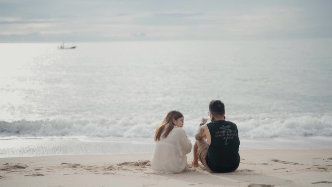 夏日夕阳下，迷人的男女坐在沙滩上庆祝周年蜜月旅行