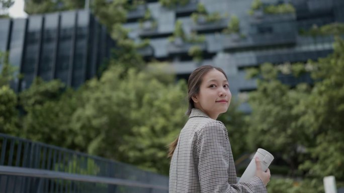 亚洲女商人走在现代都市，面对镜头微笑