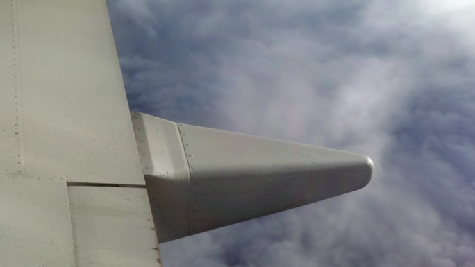 飞机的机翼飞过云层，从飞机的窗户看出去