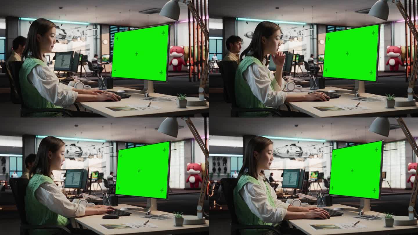 富有创造力的亚洲女性坐在她的办公桌前使用桌面电脑与绿屏Chromakey模型。在游戏设计工作室Div