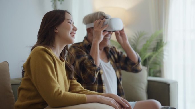 快乐的亚洲老人在与家人的空闲时间在客厅使用虚拟现实模拟器。