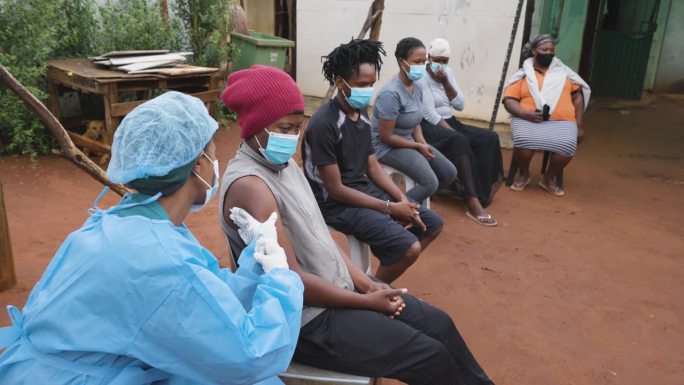 非洲黑人坐在农村诊所外等待治疗。黑人女护士正在给病人注射